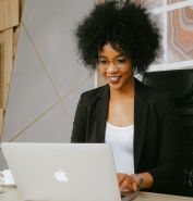 Woman in Black Blazer Sitting by the Table While Using Macbook